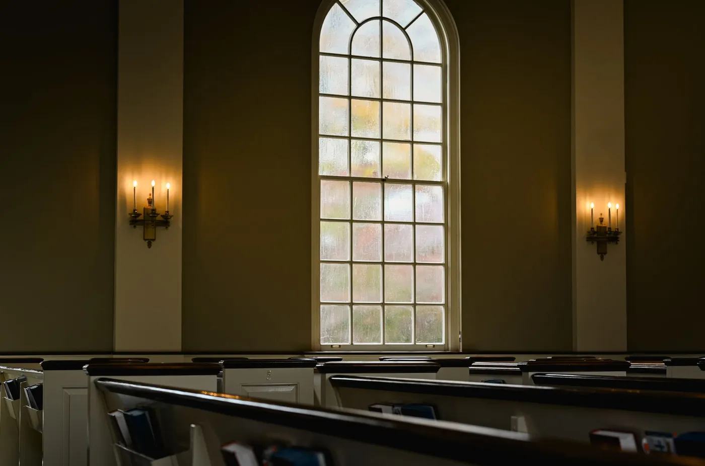 An empty church sanctuary with candles lit on the walls and daylight coming through a tall arched window