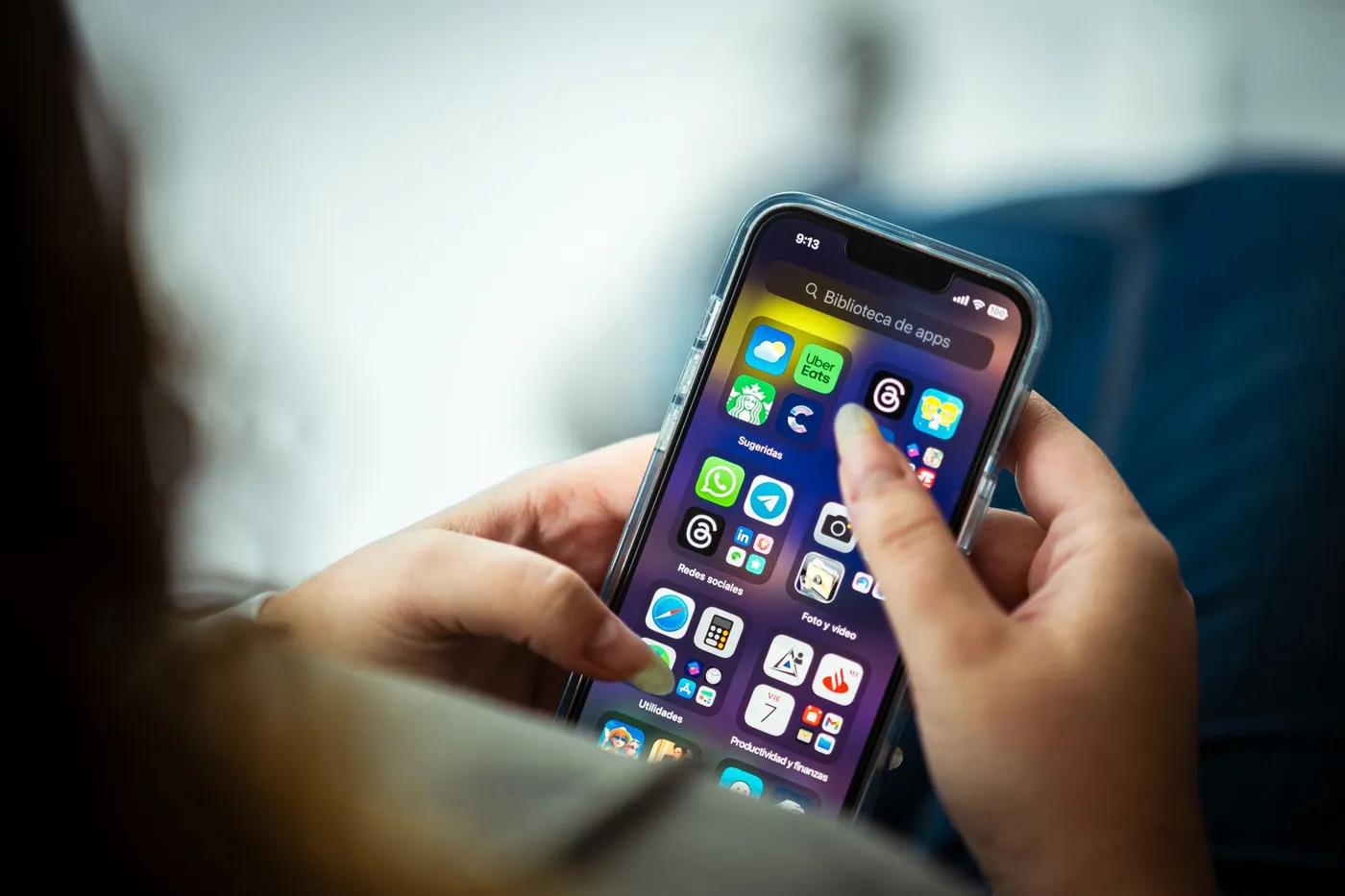 A person holding an iPhone, the home screen filled with app icons.