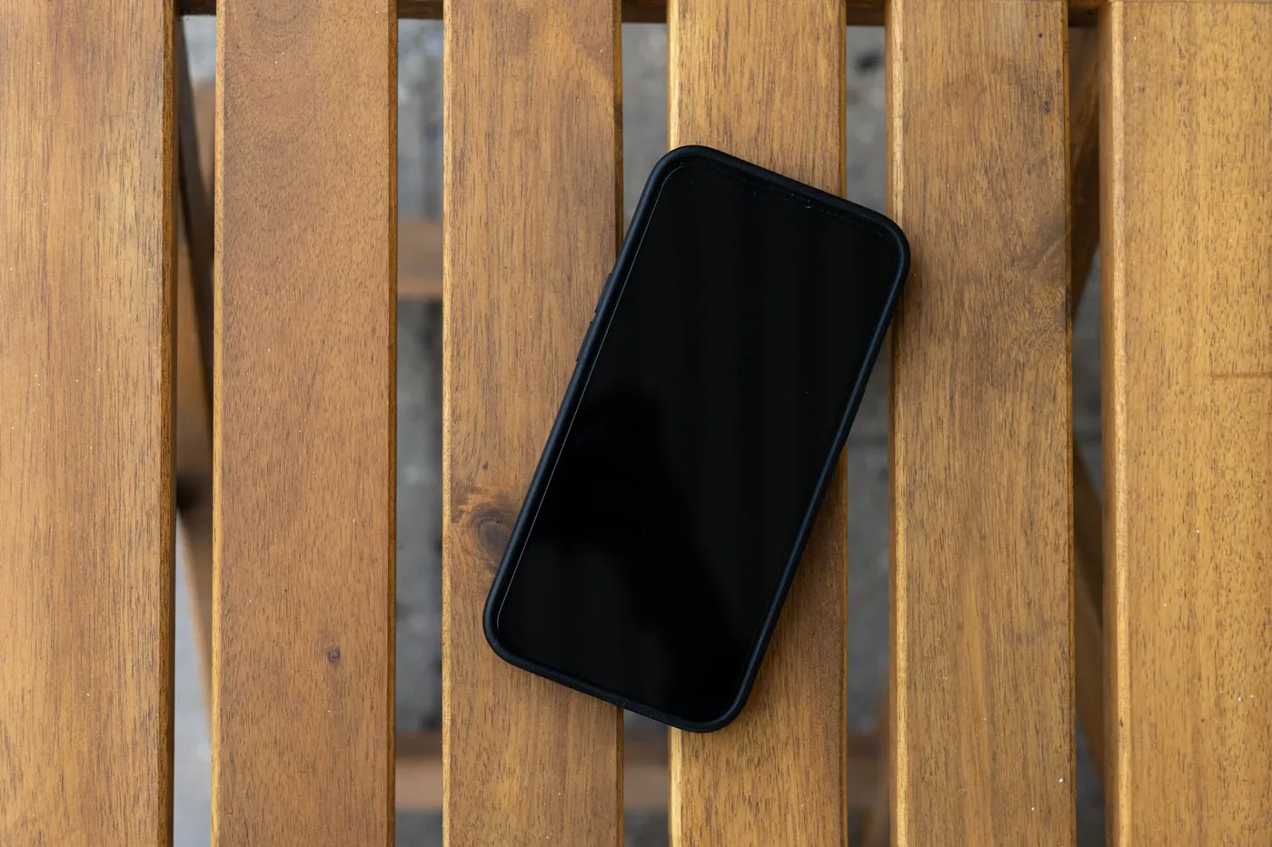 A smartphone lying face up with a dark, switched-off screen on a slatted wooden table.