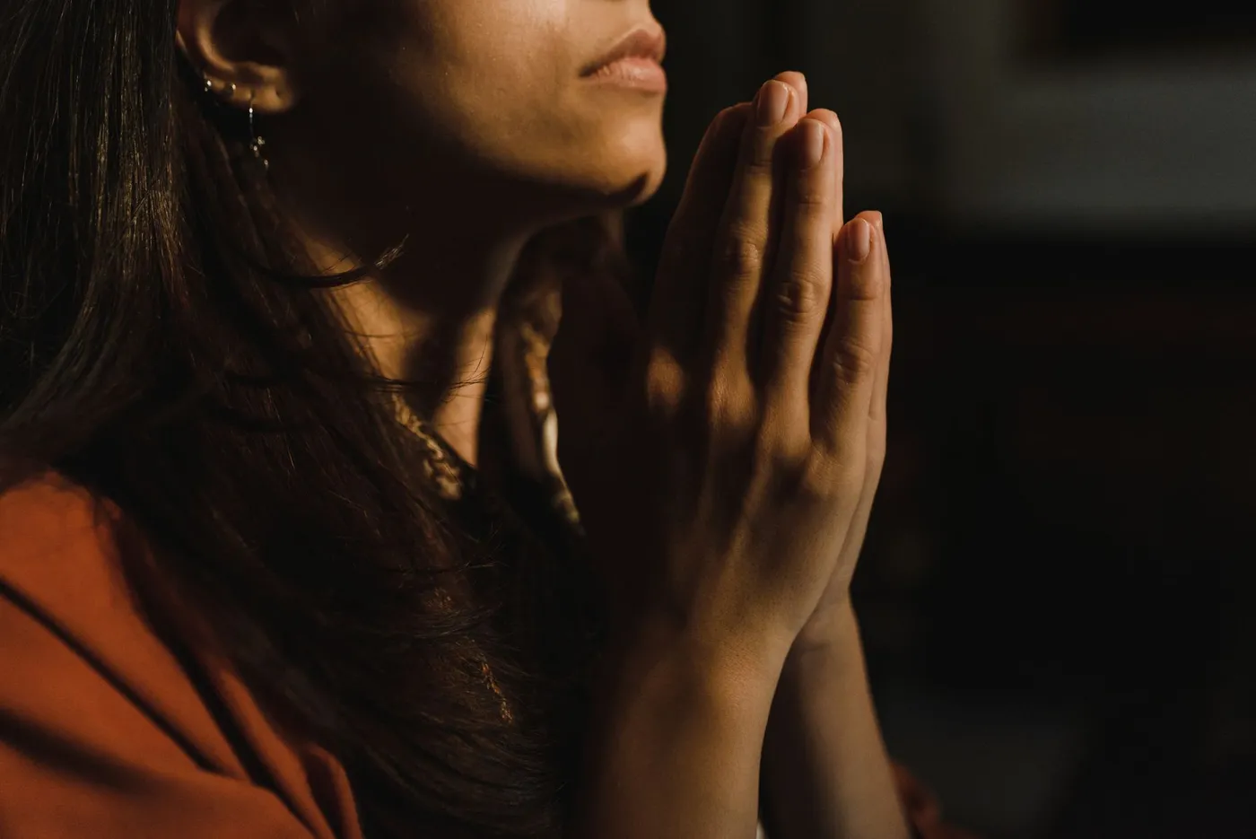 A person in an orange shirt sitting with their hands folded together in prayer.