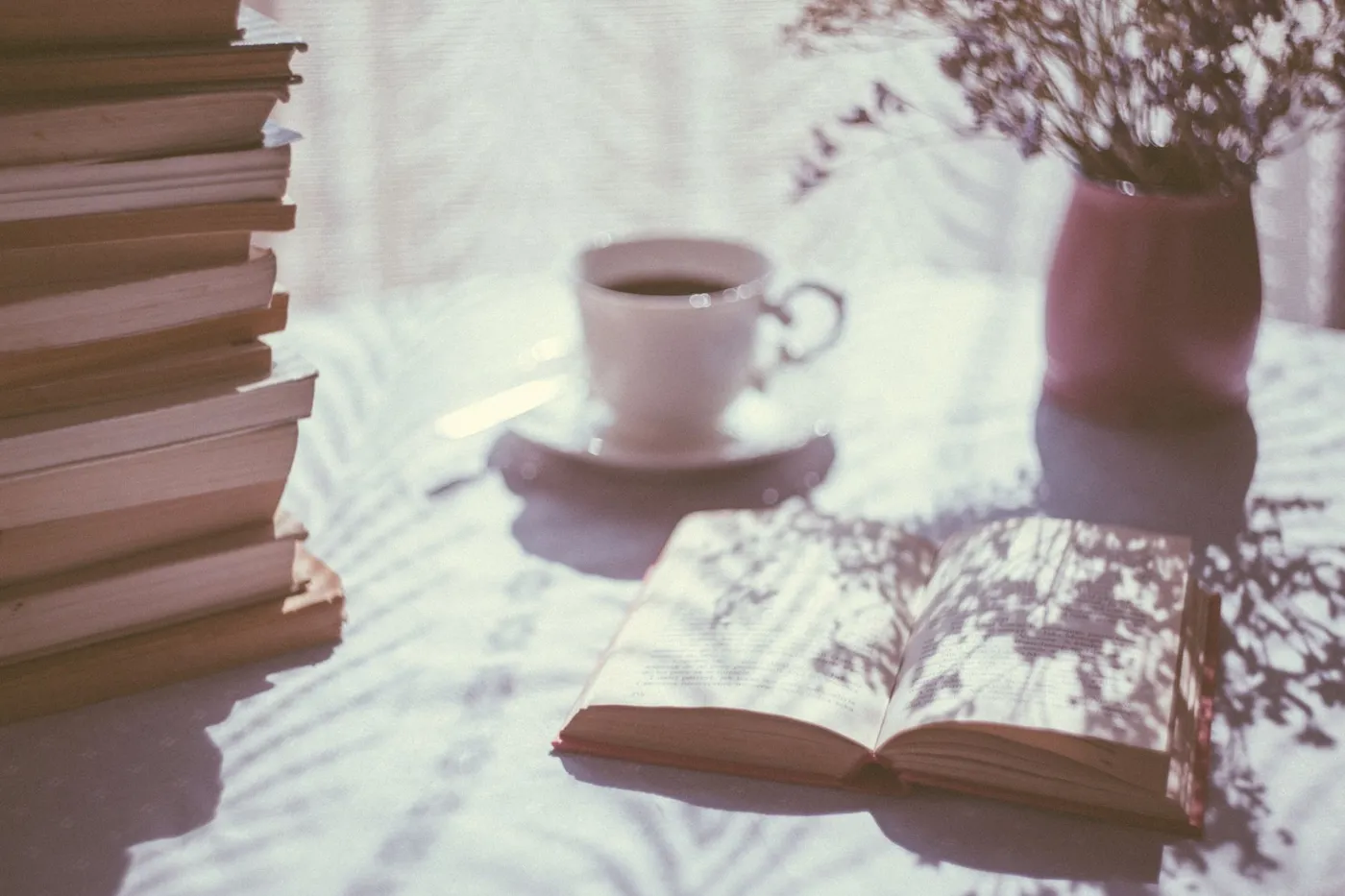 An open book lying next to a white ceramic mug of coffee on a table.
