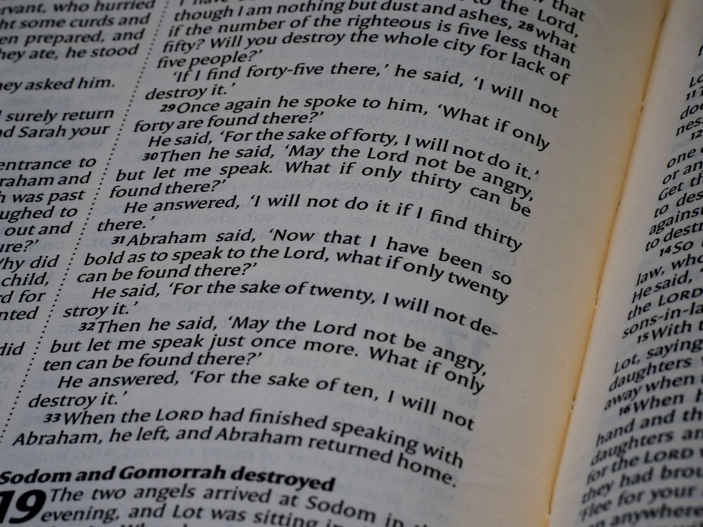 A close-up of an open Bible showing Genesis 18, where Abraham bargains with God over Sodom