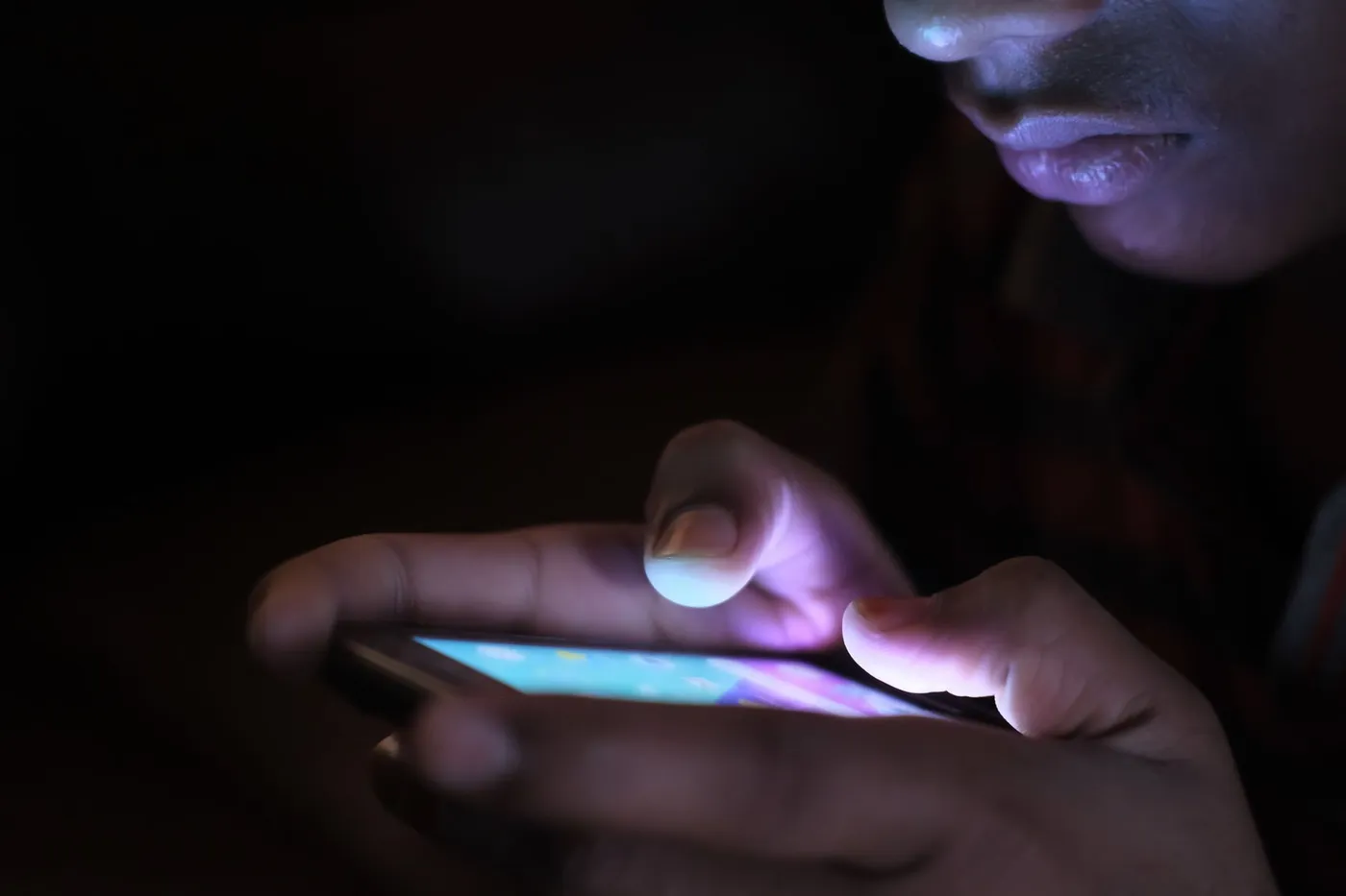A person's face lit only by the screen of the phone they are holding in the dark