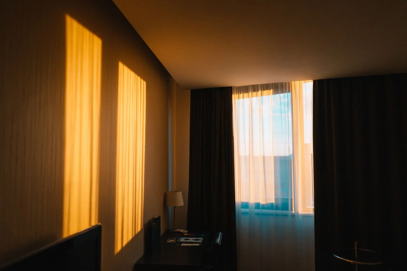 Early morning sunlight falling in bright rectangles across the wall of a quiet room with a desk and a lamp beside a curtained window