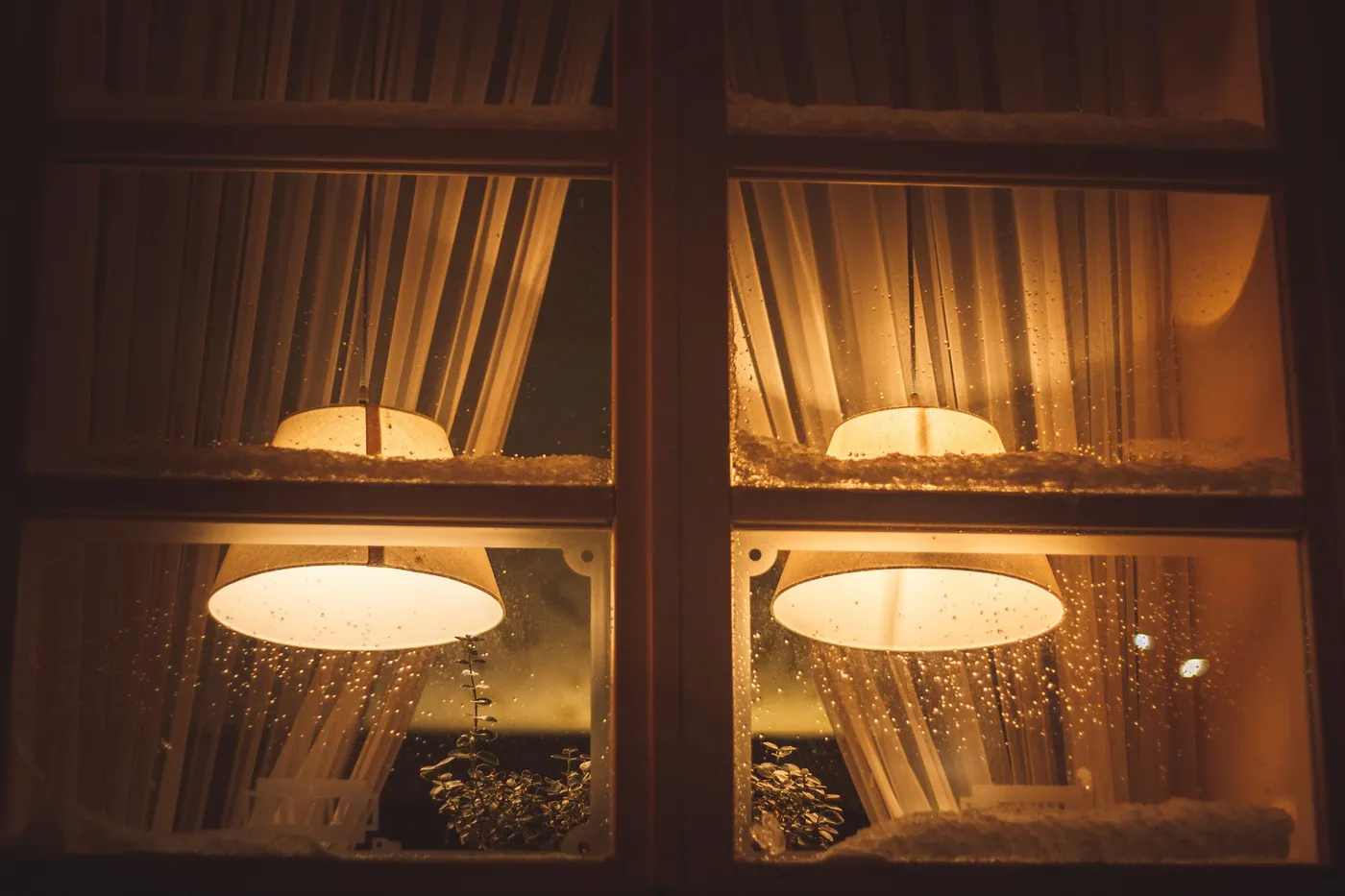 Two warm pendant lamps glowing through the panes of a snow-dusted window at night