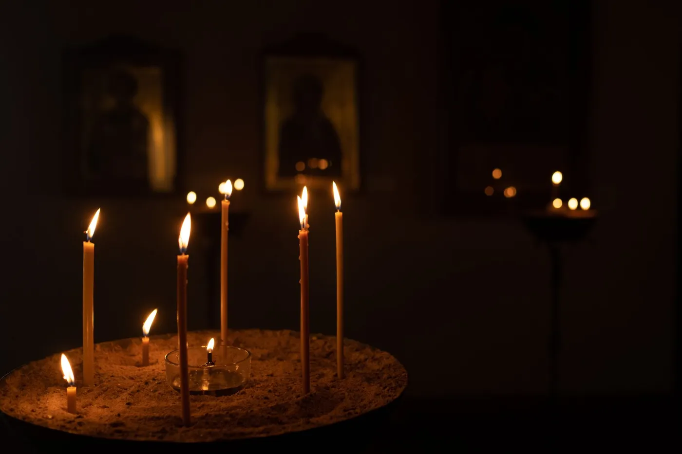 Thin beeswax candles burning in a tray of sand before dimly lit icons in an Orthodox church
