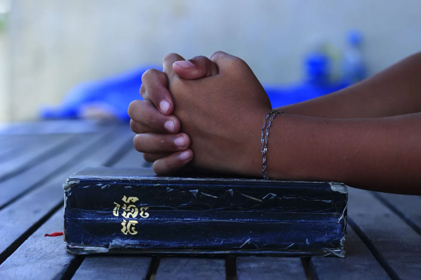 A pair of hands folded on top of a worn, taped-up hardback Bible resting on a wooden table
