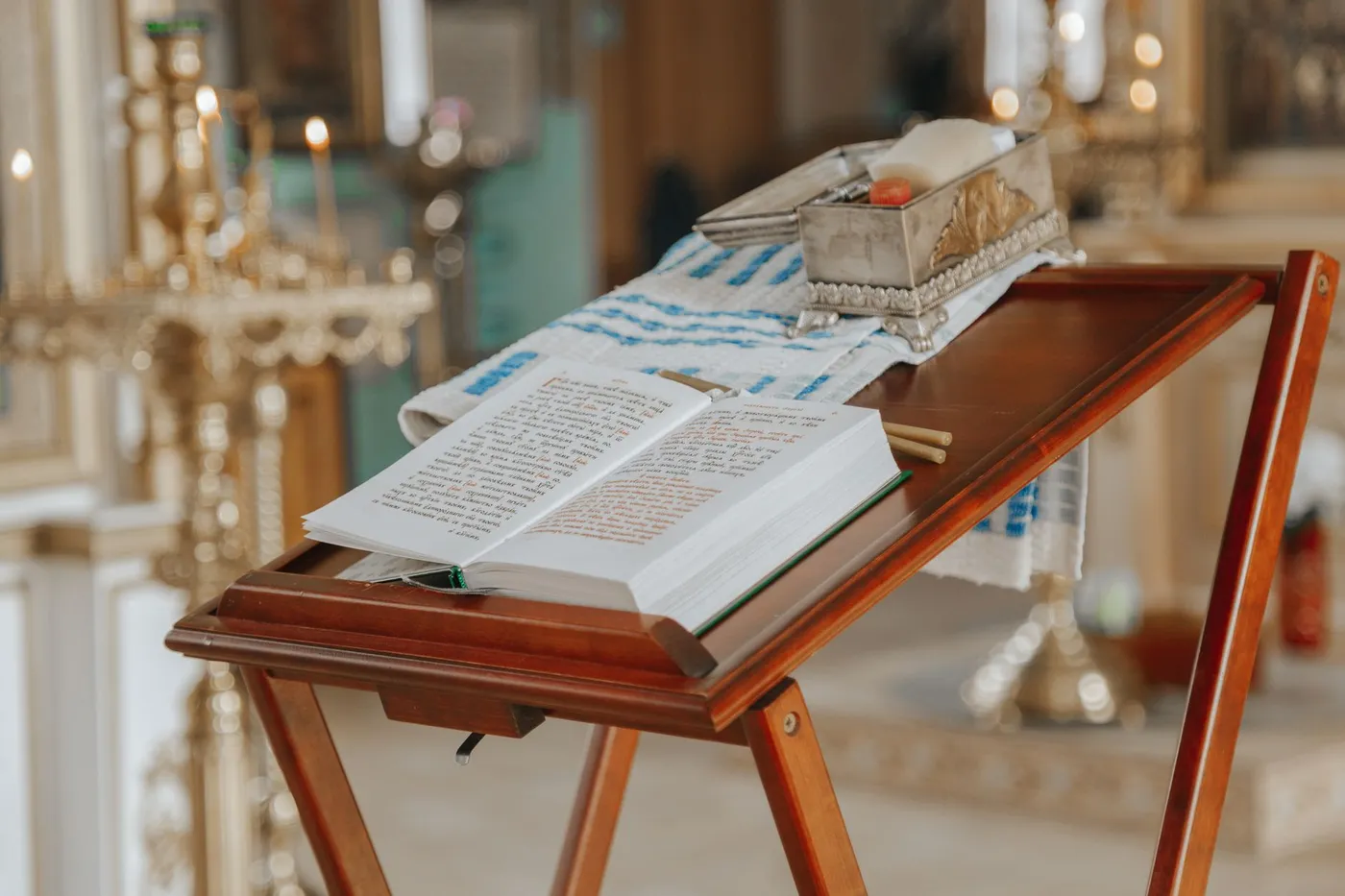 An open liturgical book on a wooden analogion in an Orthodox church, with candles behind it