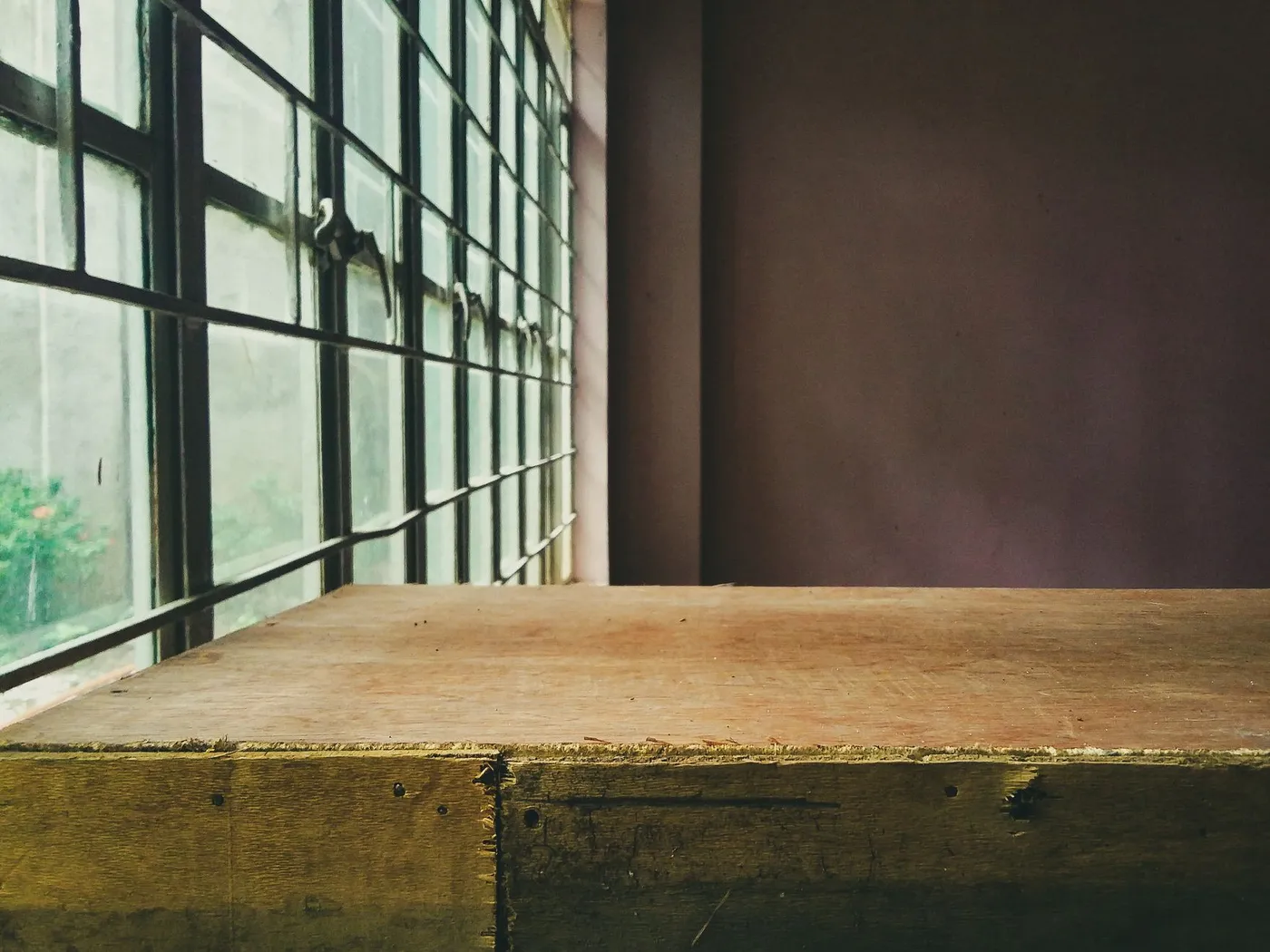 A bare wooden table beside a window of small panes in an otherwise empty room