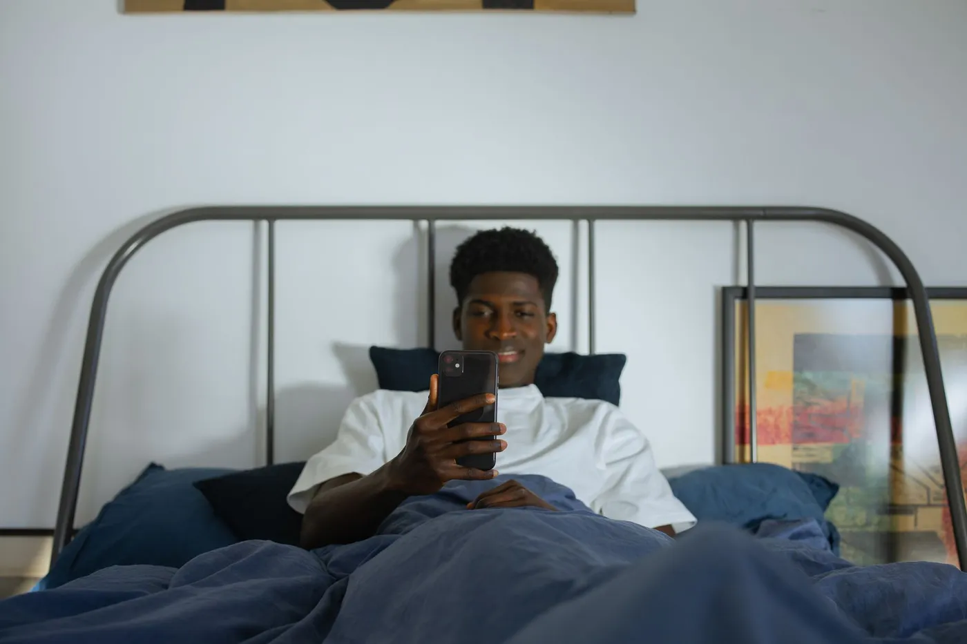 A young man lying in bed looking at his phone