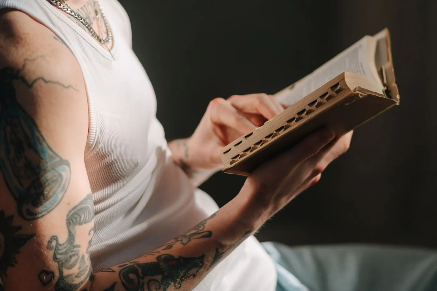A person in a white vest holding an open thumb-indexed Bible